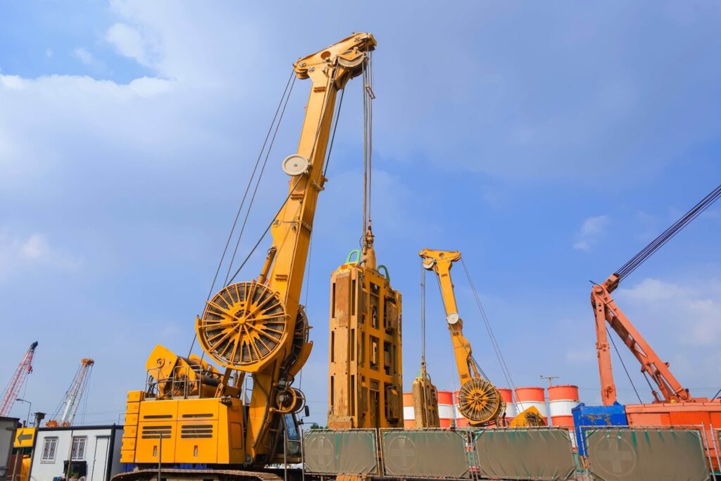 Large yellow construction cranes operate at a worksite under a blue sky, where project logistics experts coordinate industrial equipment and barriers in the background.