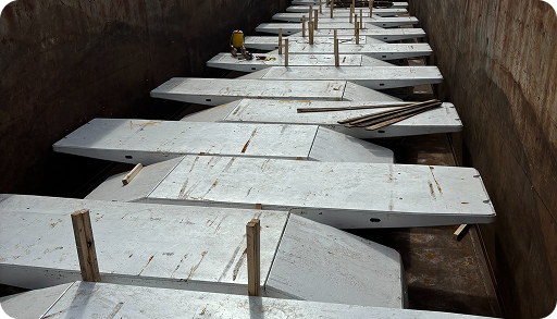 Several large, white, rectangular panels are arranged in a staggered pattern inside a metal container, with wooden supports and construction tools scattered throughout the space.